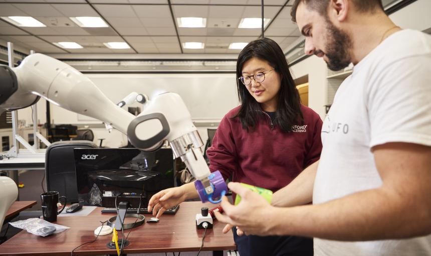 Two researchers, a woman and a man, work on a robotic arm.