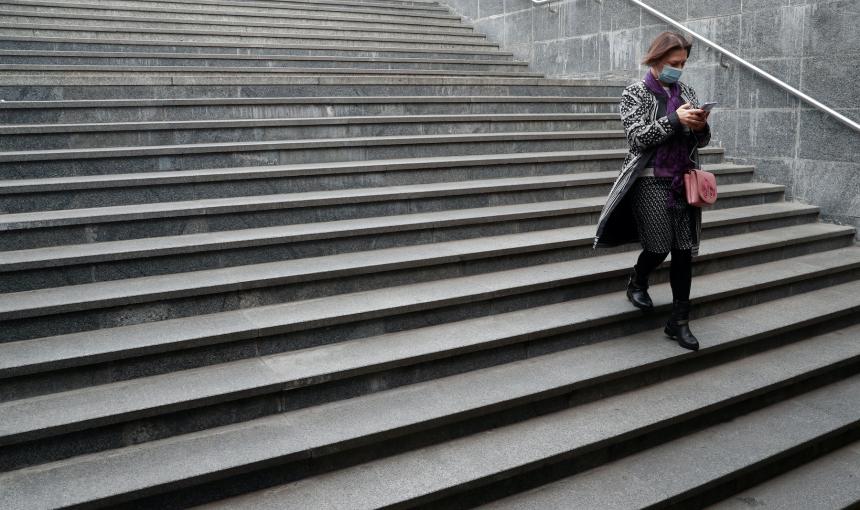 A woman walks down a lonely set of stairs while staring at her phone.