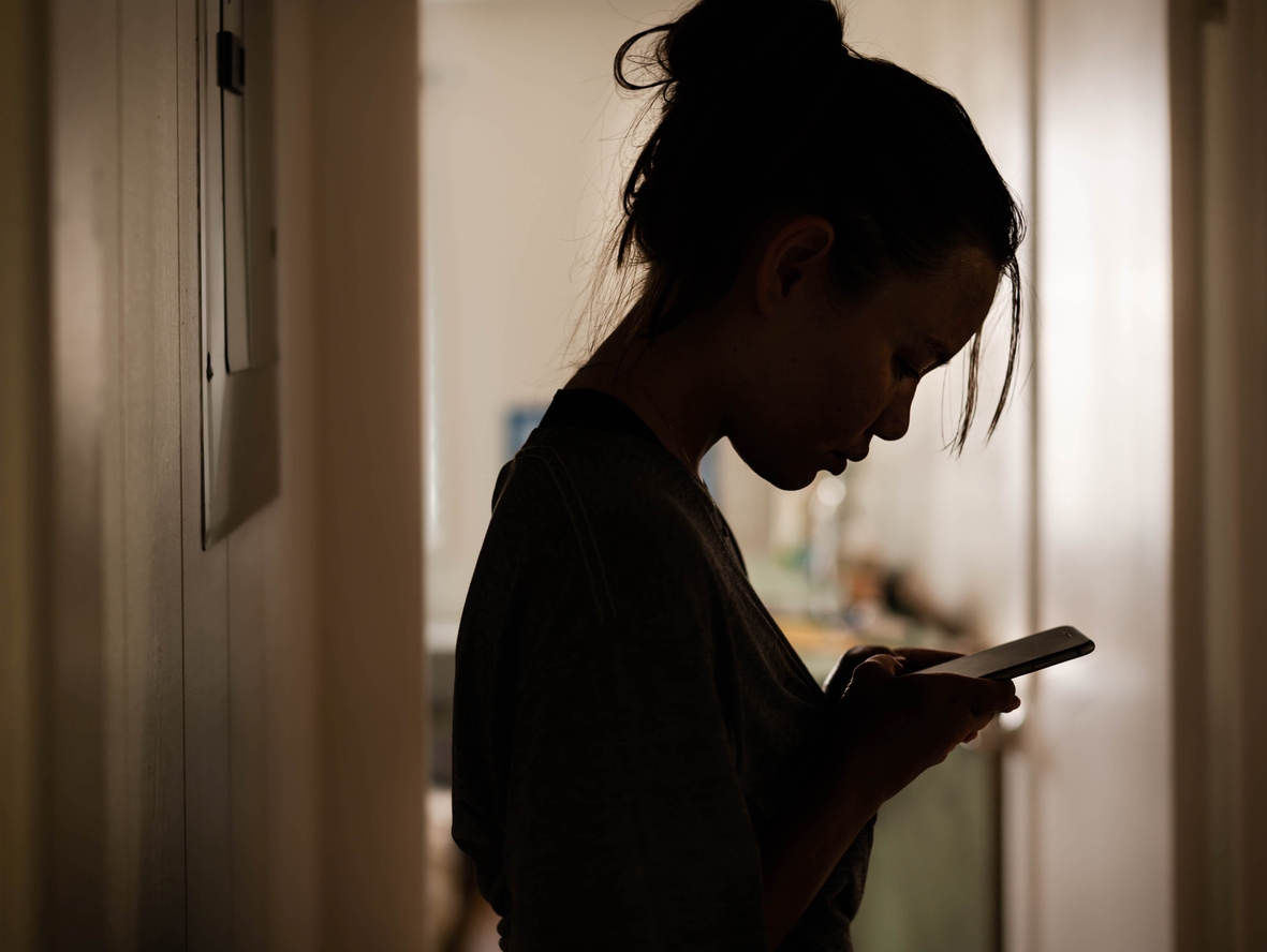 A woman looks at her phone in shadow, evoking feelings of loneliness