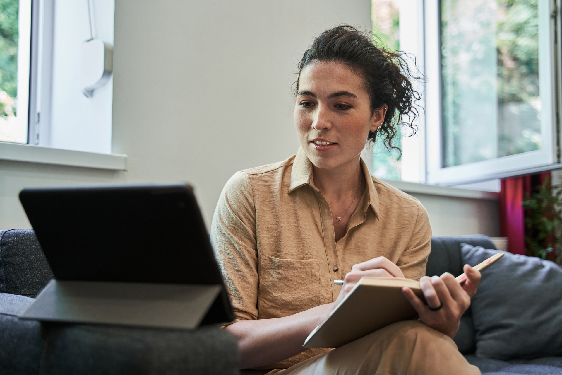 A woman takes notes while working on a tablet
