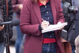 journalist holds pen and paper taking notes at a press conference