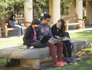 Three Stanford students sit on a bench and look at a computer together.