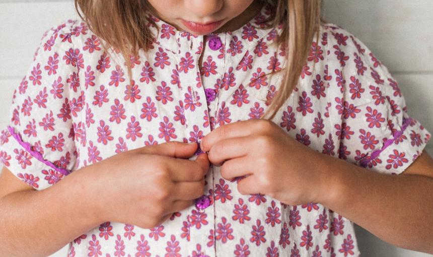 A child buttons her brightly colored flowered shirt