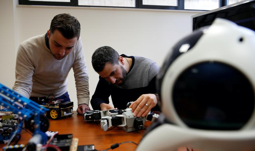 Research support officers and PhD students Luca Bondin and Foaad Haddad lean over a desk filled with robotics equipment as they work on an artificial intelligence project.