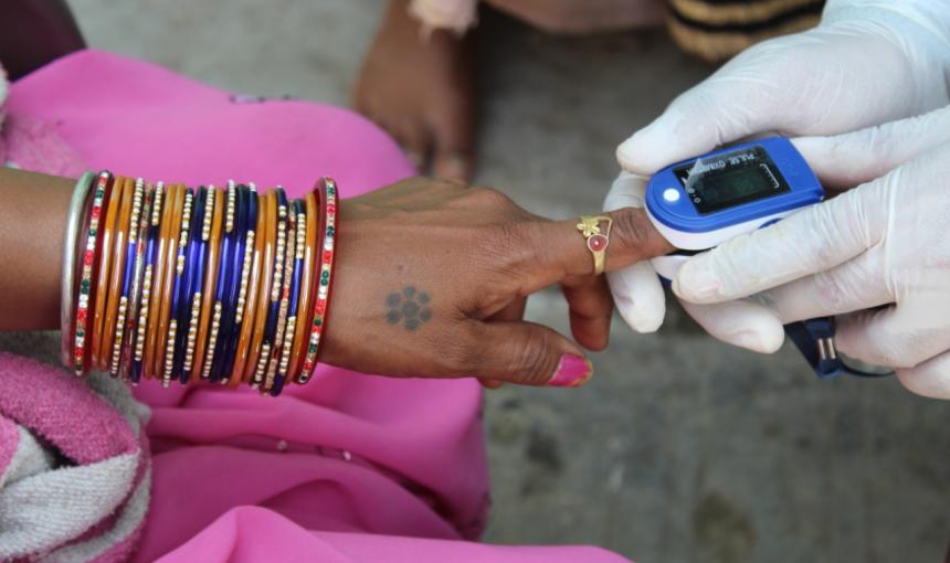 A woman's arm, lined in bracelets, as a doctor takes an oxygen reading from her index finger. 