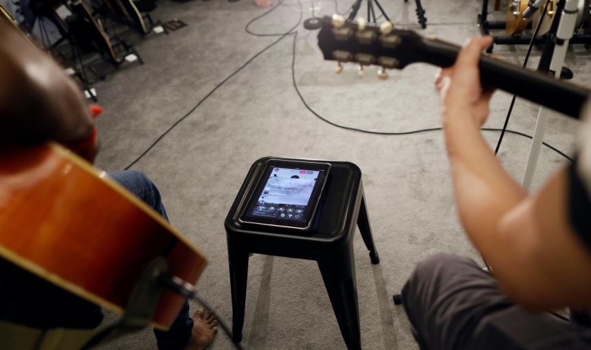 Guitarists perform with a computer tablet set up to help them record and stream.