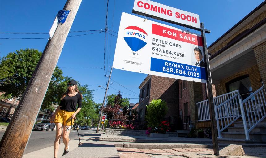 A woman walks by a for sale sign on a home in Toronto.