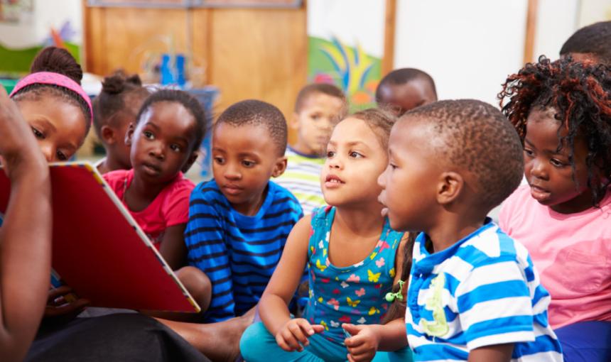 Children are read to by an instructor in a classroom. 