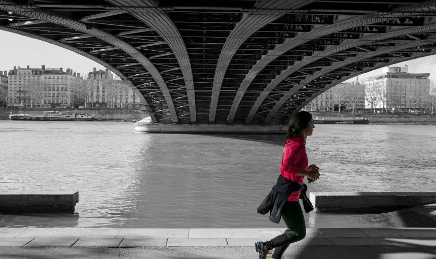 A woman jogs down a path under a bridge