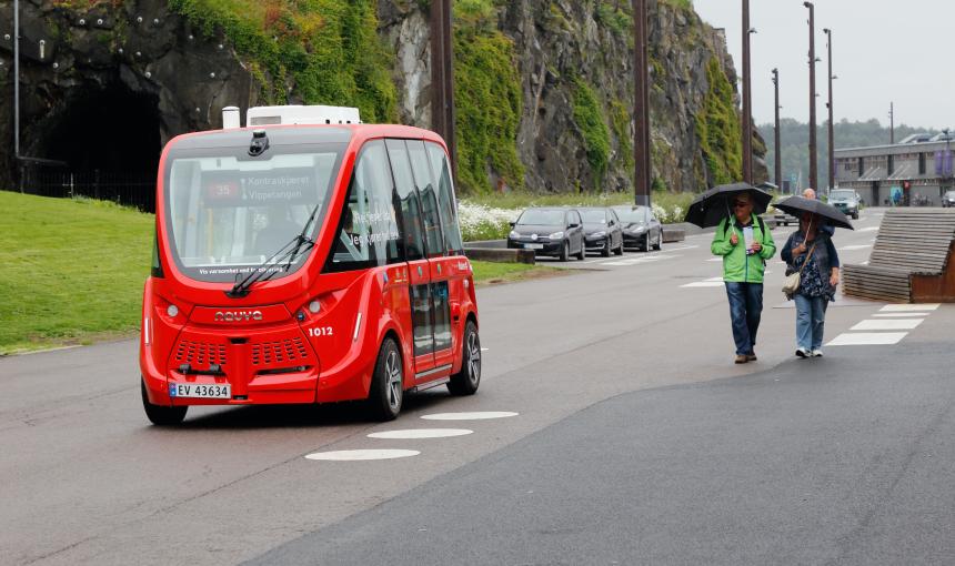 An autonomous bus passes two pedestrians in Oslo, Norway.