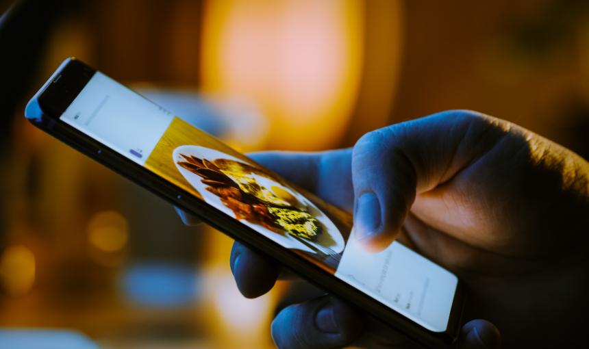 Close-up Macro: Person Holding and Using Smartphone, Browsing through Pictures on Social Network Wall.