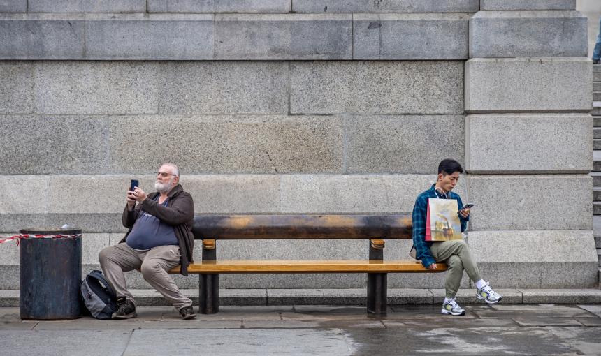 Two men on a bench - one mature European and one young Asian with their mobile phones