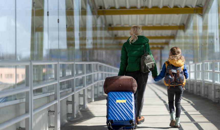 A Ukrainian mother and daughter walk through an airport with their luggage.
