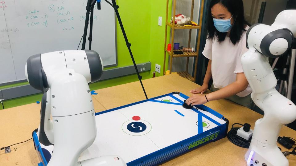 A doctoral student plays air hockey against a robotic arm