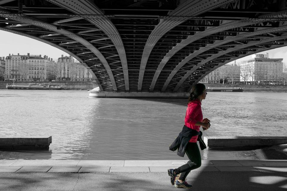 A woman jogs down a path under a bridge. 