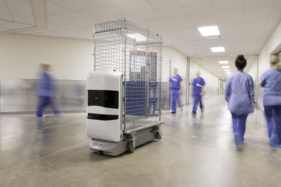 A robot carrying medical supplies rolls down a crowded hospital hallway. 