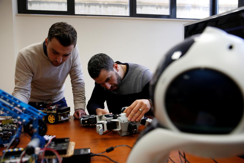 Research support officers and PhD students Luca Bondin and Foaad Haddad lean over a desk filled with robotics equipment as they work on an artificial intelligence project.