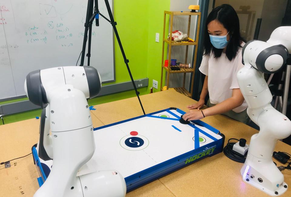 A doctoral student plays air hockey against a robotic arm