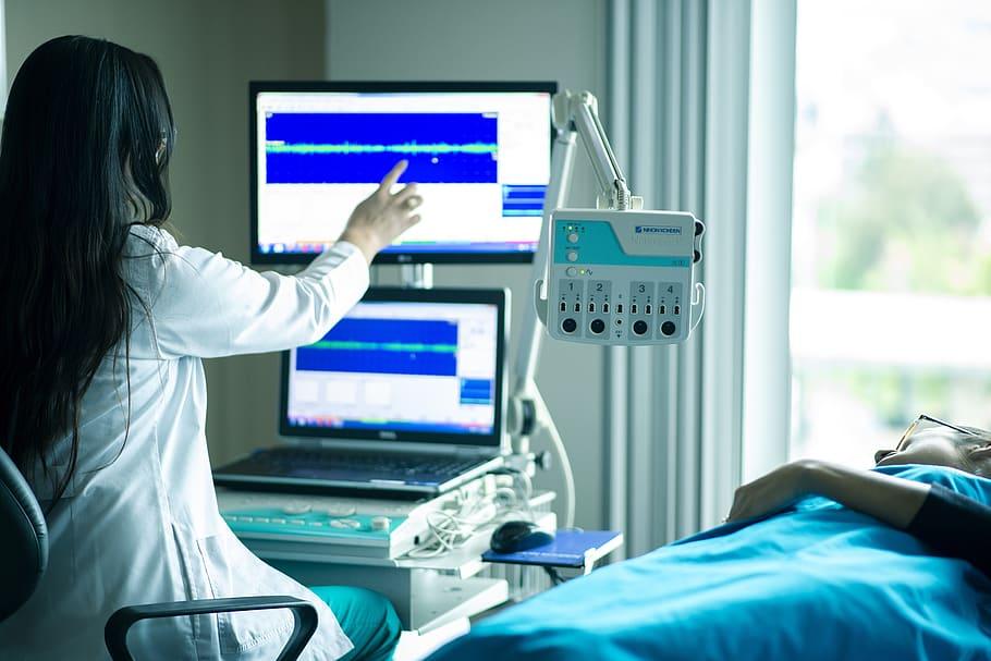 A doctor looks like a computer screen next to a patient in a hospital bed.