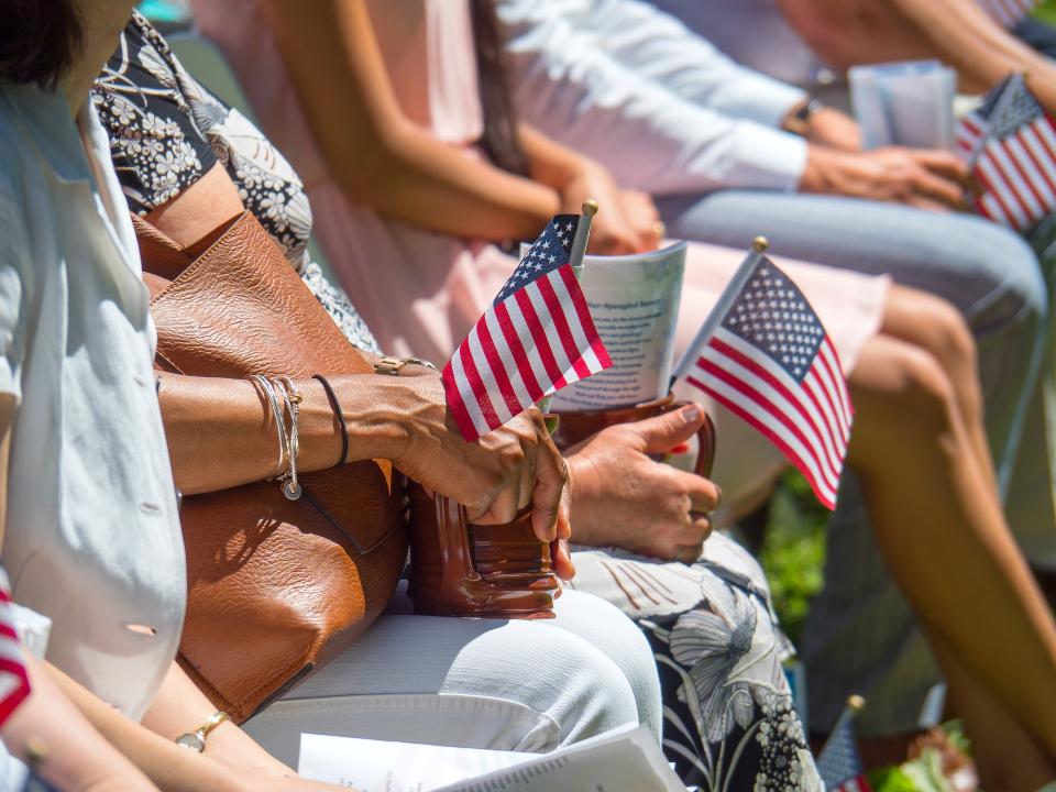 People sit outside, the photo focused at the hands in their laps, holding coffee mugs and American flags