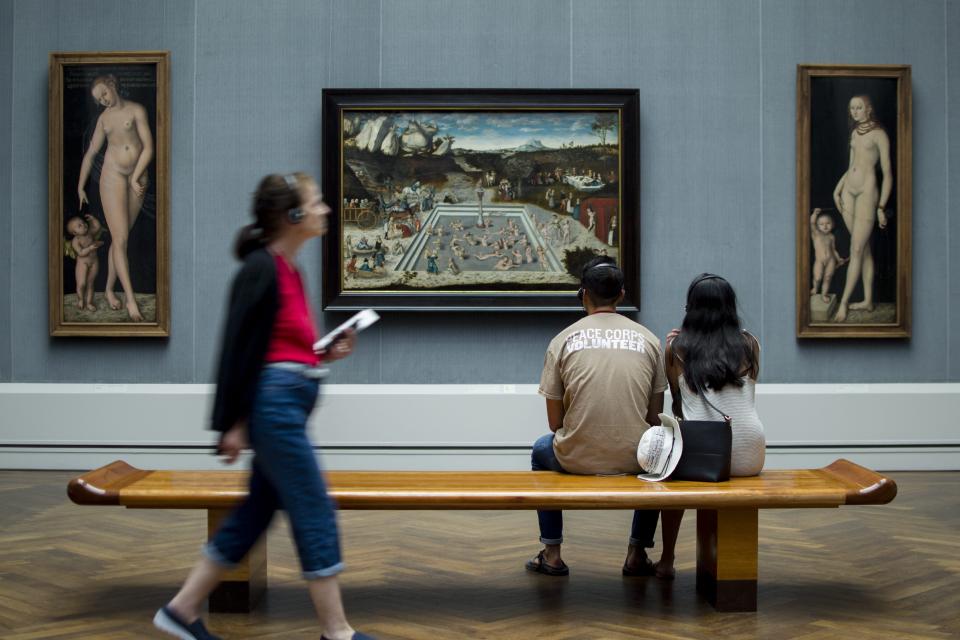 A couple sit on a bench in a museum looking at a work of art.