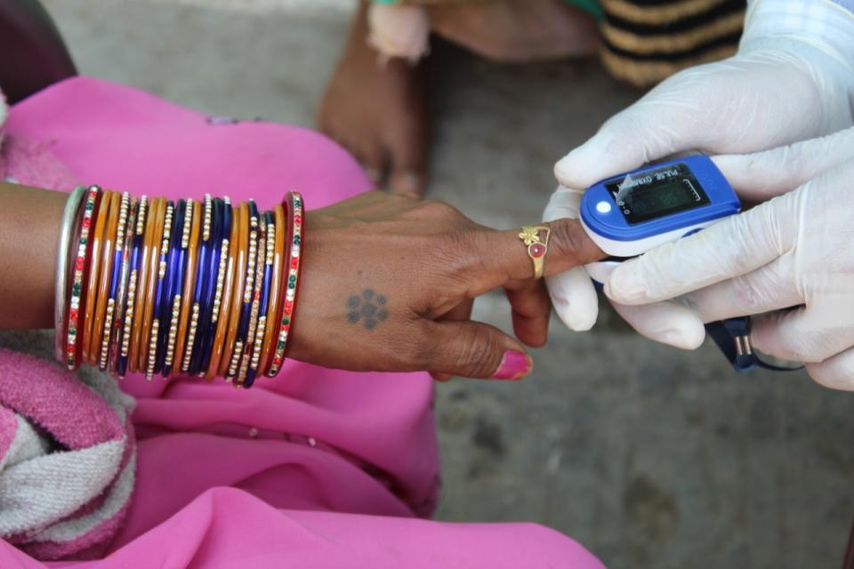 A woman's arm, lined in bracelets, as a doctor takes an oxygen reading from her index finger. 