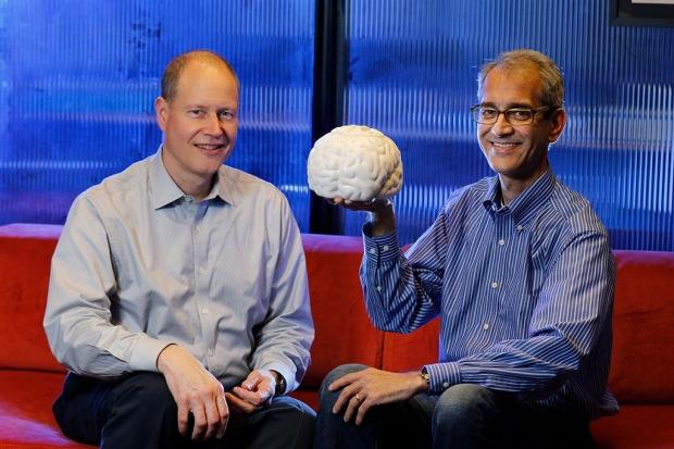 Jaimie Henderson, left, sits with Krishna Shenoy on a couch holding a model of a brain.
