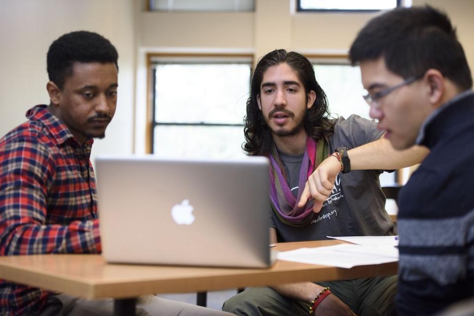 Three student researchers discuss their work while looking at a computer and sitting at a table. 