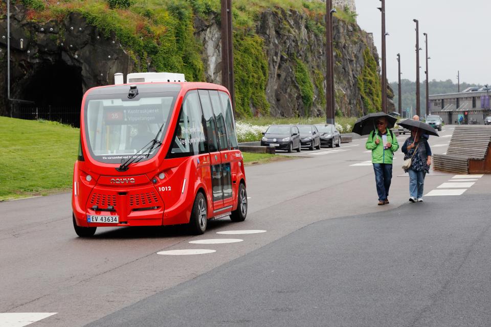 An autonomous bus passes two pedestrians in Oslo, Norway.