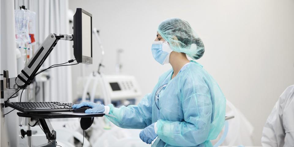 A health care worker in full scrubs looks at a computer screen.