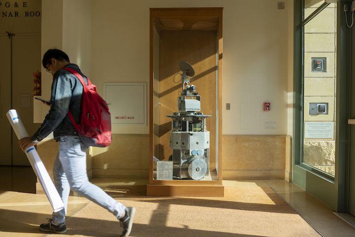 mobi the robot sits in a glass case in a hallway as a student walks by