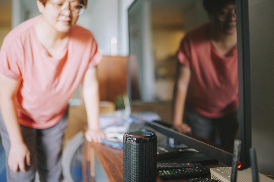 An older woman speaking to her smart speaker in living room turn on music