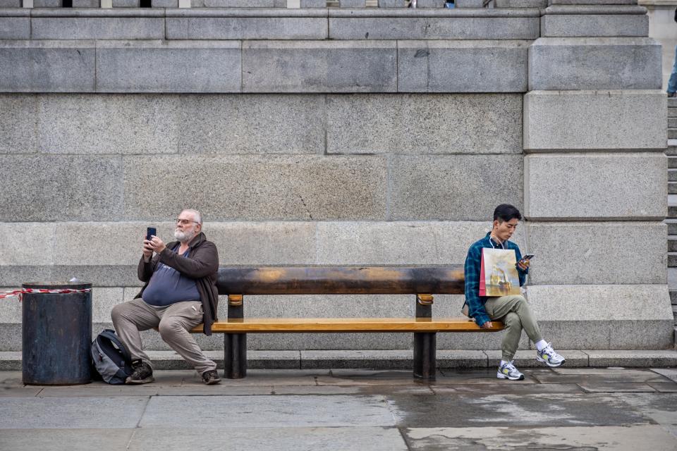 Two men on a bench - one mature European and one young Asian with their mobile phones