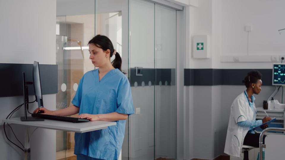 Front view of assistant typing medical expertise on computer while in background practitioner talking with a patient