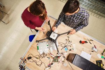 2 students huddle around a table to work on a drone together